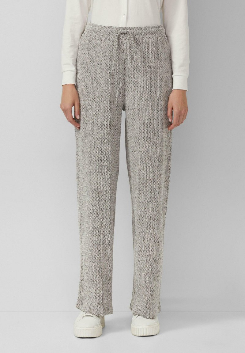 Hellgraue Strickhosen mit einem Kordelzugbund, lockerer Passform und strukturiertem Stoff. Getragen mit weißen Turnschuhen für einen lässigen Look.