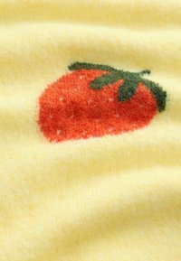 Tissu jaune doux avec une fraise rouge et des feuilles vertes tricotées dans le matériau, montrant des détails de texture et de couleur.