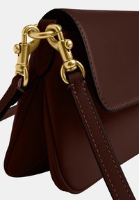 Sac à main en cuir marron foncé avec des bords cousus et un fermoir en métal doré fixant la bandoulière au corps du sac.