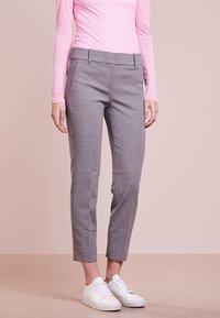 Pantalon gris clair sur mesure avec une texture lisse, coupe slim et jambes fuselées. Détail avec des poches plates à l'avant, porté avec des baskets blanches.
