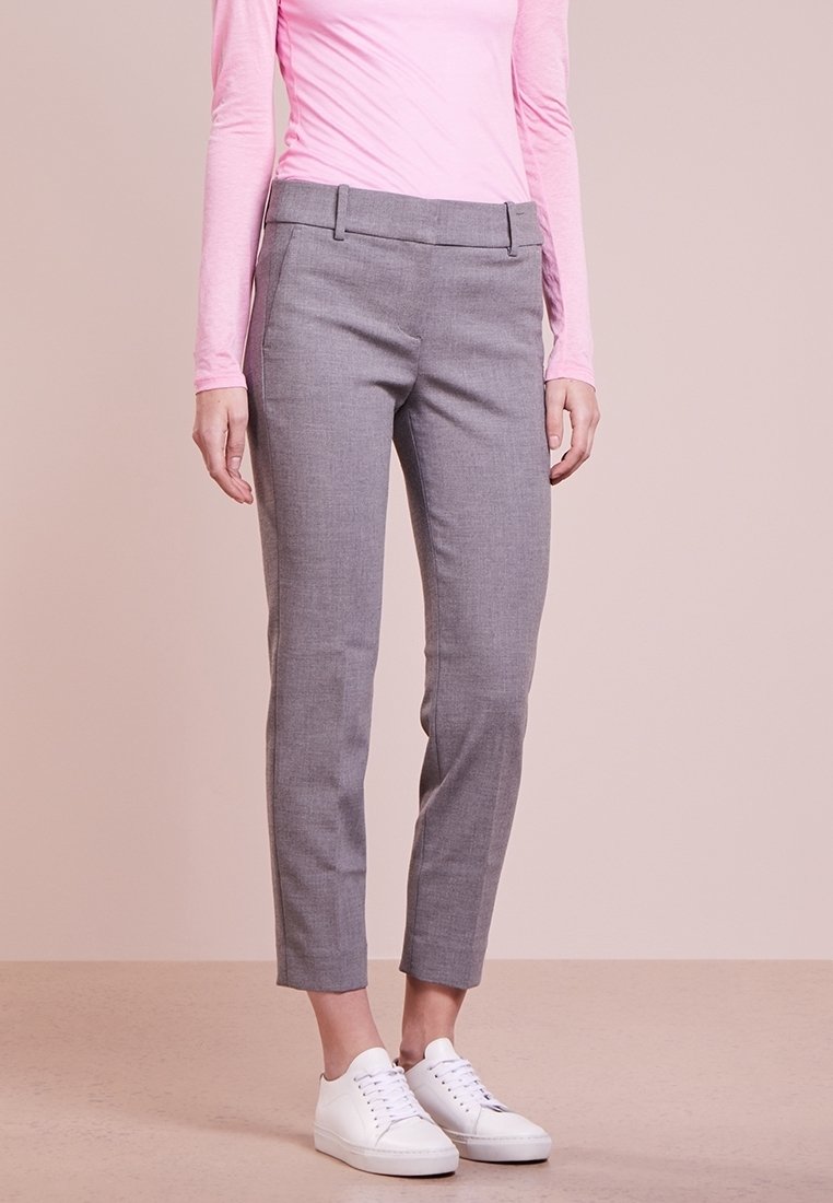 Pantalon gris clair sur mesure avec une texture lisse, coupe slim et jambes fuselées. Détail avec des poches plates à l'avant, porté avec des baskets blanches.