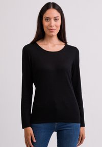 Schwarzes Langarmoberteil mit rundem Halsausschnitt. Hergestellt aus einem weichen, strukturierten Stoff, hat es eine schmale Passform, die sich an der Taille verjüngt. Kombiniert mit blauen Jeans.