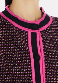 Giacca in tweed caratterizzata da una combinazione di colori viola, rosa e nero, accentuata da fili metallici, colletto rosa e bottoni decorativi.