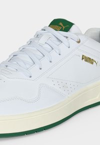 Hvid Puma-sneakers med gyldent logo, hvide snørebånd, grøn tungeetiket og grøn detalje på ydersålen, der viser side- og frontøvre sektioner.
