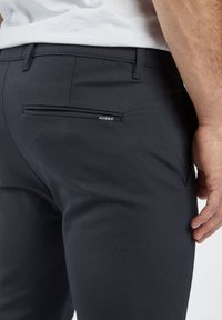 Dark gray trousers featuring a textured fabric with a subtle dotted pattern. Includes a back pocket with a branded label.