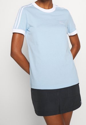 Person wearing a light blue Adidas t-shirt with white trim and stripes, paired with a black mini skirt.