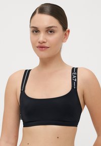 Fekete sportmellény széles pántokkal, fehér részletekkel. Simás anyag, letisztult dizájn, ami cropped sziluettet biztosít.
