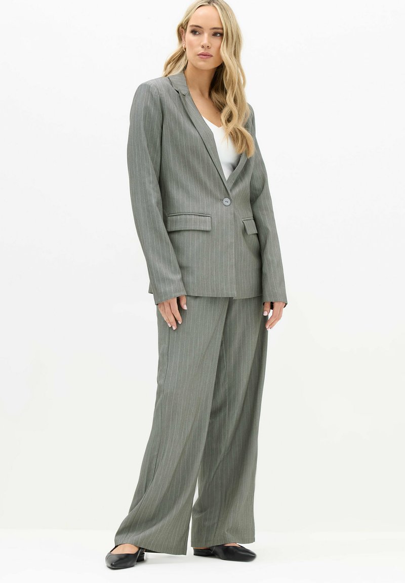 Grijs gestreept pak met een getailleerde blazer en wijde broeken. De stof lijkt textuur te hebben; de blazer heeft een enkele knop en twee zakken.