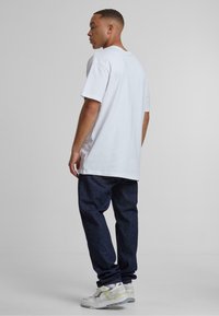 Camiseta de algodón blanca con mangas cortas, de corte relajado, combinada con jeans de denim oscuro y zapatillas ligeras con detalles en gris y amarillo.