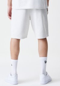 Gray cotton shorts with a loose fit, featuring side pockets. Worn with white socks and white sneakers, displaying subtle brand logo on socks.