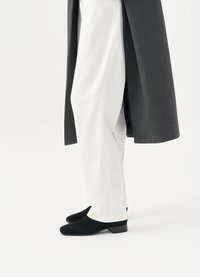 Černé semišové boty, bílé přizpůsobené kalhoty a tmavě šedý dlouhý kabát, zdůrazňující elegantní a štíhlý vzhled.