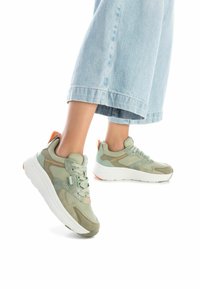 Zapatillas verde claro con materiales de malla y ante, que cuentan con un acento naranja, suela blanca gruesa y detalles texturizados en la parte superior.
