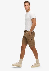 Beige cargo shorts med fire lommer, parret med en tætsiddende hvid t-shirt. Båret med lyse sneakers og uldblandede sokker.