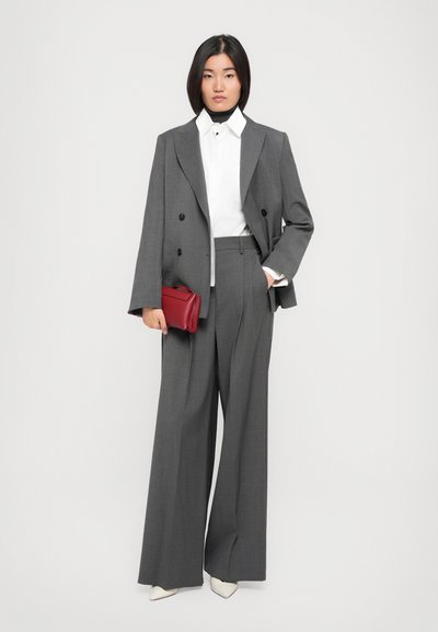 Giacca elegante grigia doppiopetto e pantaloni a gamba larga, abbinati a una camicia bianca. Borsa a tracolla rossa, tacchi bianchi a punta.