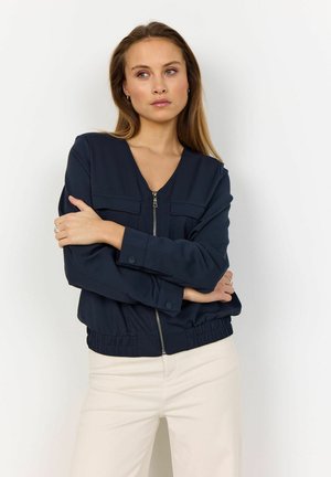 Veste cropped marine avec fermeture éclair sur le devant, deux poches poitrine et taille élastique ; fabriquée en tissu lisse avec un léger éclat.