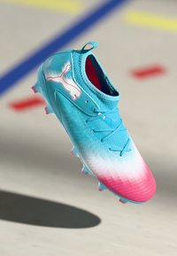 Scarpino da calcio blu chiaro e rosa con una parte superiore texture, chiusura con lacci e suola chiodata. Logo Puma bianco sul lato esterno.