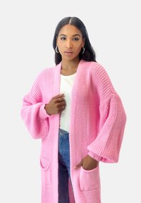 Lång, öppen cardigan i strukturerad rosa stickad material. Har överdimensionerade ärmar, sidfickor och en avslappnad passform.
