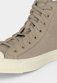 Μπεζ ψηλοτάκουνο αθλητικό παπούτσι με υφασμάτινο άνω μέρος με υφή, κορδόνια στο ίδιο χρώμα, μεταλλικά κορδόνια και εκρού λαστιχένια σόλα και μύτη.