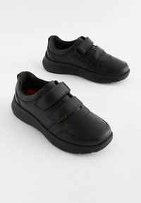 Zapatos de cuero negro con dobles correas de Velcro, punta redondeada, suela texturizada y un acolchado en el cuello para mayor comodidad.