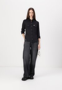Black button-up shirt with two chest pockets and a textured pattern, paired with wide-leg dark grey jeans and chunky black shoes.