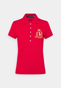 Polo shirt rouge avec un col pointu, des manches courtes, des boutons blancs et un logo brodé en or et vert sur la poitrine gauche.
