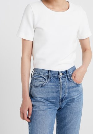 Haut blanc à manches courtes avec un col rond, en tissu côtelé, associé à un jean en denim bleu taille haute avec des poches classiques.