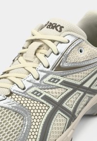Nærbilde av beige Asics-sneaker med mesh, honningkake-mønster, sølvdetaljer og kremfargede lisser.