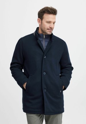 Cappotto blu navy con design con colletto, chiusura a bottoni e tasche frontali. Lo strato interno è in tessuto trapuntato blu navy. Texture liscia.