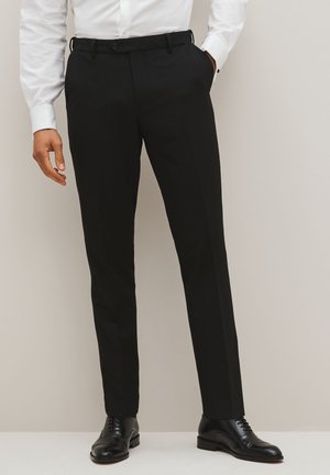 Pantaloni neri su misura con una trama liscia, design a gamba dritta e chiusura con bottone. Indossati con una camicia bianca e scarpe nere.