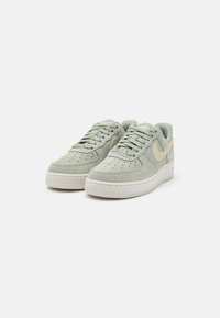 Lysegrønne semskede sneakers med en tekstureret overflade, som har en hvid gummisål og et tan Nike-swoosh. Snørebånd og perforeret tådesign er inkluderet.