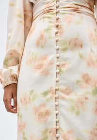 Κοντινό πλάνο ενός φορέματος με λουλούδια, μακριά μανίκια και κουμπιά καλυμμένα με ύφασμα που τρέχουν κάθετα στο κέντρο μπροστά.