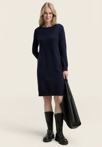 Rochie bleumarin tricotată cu mâneci lungi și tiv cu dungi, asortată cu cizme negre de cauciuc până la genunchi și o geantă tote mare neagră.