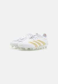 Botas de fútbol blancas con acentos dorados, que presentan un upper texturizado, un ajuste ceñido y tacos multidireccionales para una mejor tracción en el campo.