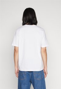Tricou alb din bumbac, cu mâneci scurte, guler rotund și croială dreaptă. Vedere din spate fără grafice sau modele vizibile.