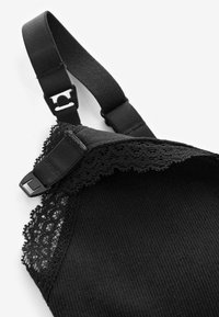 Reggiseno nero con bordi in pizzo e spalline regolabili, caratterizzato da una morbida texture a costine e una chiusura in plastica per un fissaggio sicuro.