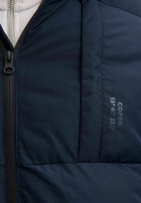 Chaqueta de plumas azul marino con cierre de cremallera, textura acolchada y un detalle de coordenadas impreso en la tela. Forro interior suave.