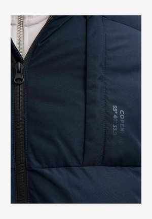 Tumši zilā pūkainā jaka ar rāvējslēdzēju, iešūtu tekstūru un apdrukātu koordinātu detaļu uz auduma. Gluda iekšējā odere.