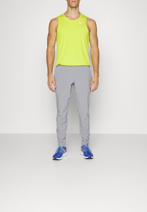 Helles gelbes ärmelloses Sportoberteil, graue tapered Hose und blaue Laufschuhe mit gemusterten Akzenten. Schlichte, funktionale Sportbekleidung.