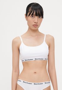 White bralette with thin straps featuring a black Juicy Couture logo band at the bottom; smooth texture, minimal design.