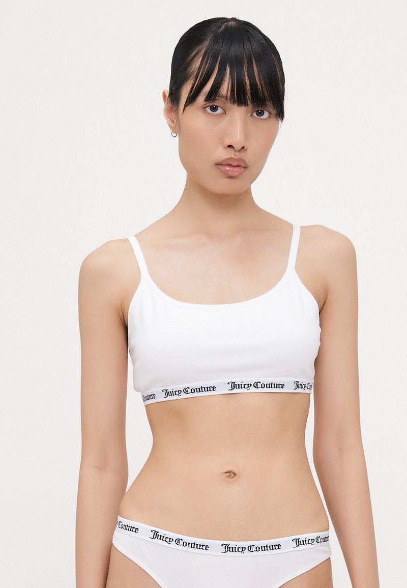 White bralette with thin straps featuring a black Juicy Couture logo band at the bottom; smooth texture, minimal design.