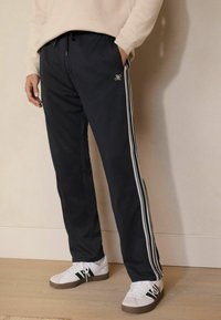 Pantalones deportivos marinos con franjas laterales blancas, cintura con cordón y un corte ajustado. Combinados con zapatillas blancas con detalles en negro.