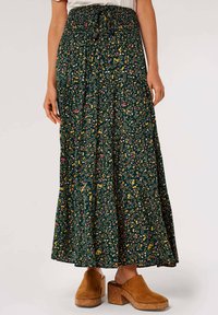 Floral maxi skirt in dark green, featuring a smocked waistband, blended small pink and yellow flowers, and a flared bottom; worn with tan clogs.