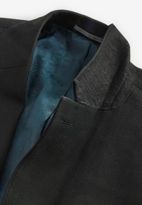 Chaqueta negra con un exterior texturizado, que presenta un cuello gris. El forro interior es de una tela de color teal con un patrón.