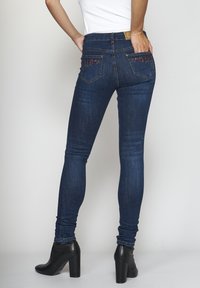 Tummansiniset farkut, jotka ovat kapea malli ja joissa on kukkakirjontaa takataskuissa. Niissä on istuva siluetti ja normaali vyötärö.