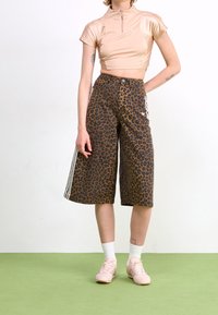 Beige crop top med dragkedja, matchad med bruna culottbyxor med leopardmönster och sidostrecken. Buren med ljusrosa sneakers och vita strumpor.