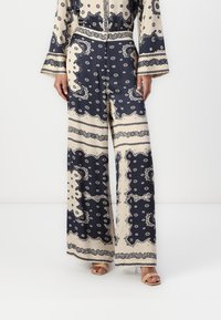 Pantaloni a gamba larga con un motivo blu navy e crema, caratterizzati da design intricati, tessuto morbido e una silhouette fluida. Presentano una chiusura con bottone in vita.