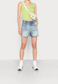 Grön tanktopp, ljusblå denimshorts, färgglad midjeväska, vita strumpor och sneakers med rosa accenter. Avslappnad sommaroutfit.