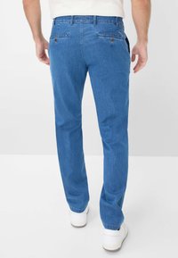 Pantaloni in denim blu con vestibilità comoda, dotati di due tasche posteriori con bottoni e un design minimalista. Sneakers bianche completano il look.