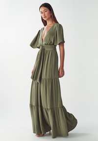 Langes olivengrünes Kleid mit tiefem V-Ausschnitt, weiten Ärmeln, taillierter Taille und gestuftem Rock. Weicher, strukturiertes Material mit fließender Silhouette.