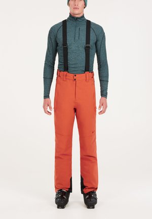 Oranje skibroek met zwarte bretels, gladde textuur, met ritszakken en versterkte stukken bij de enkels, gecombineerd met een blauwe top.